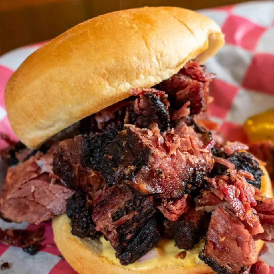 A Little Russia Chili Parlor sandwich, overflowing with dark, shredded meat on a bun, on checkered paper.