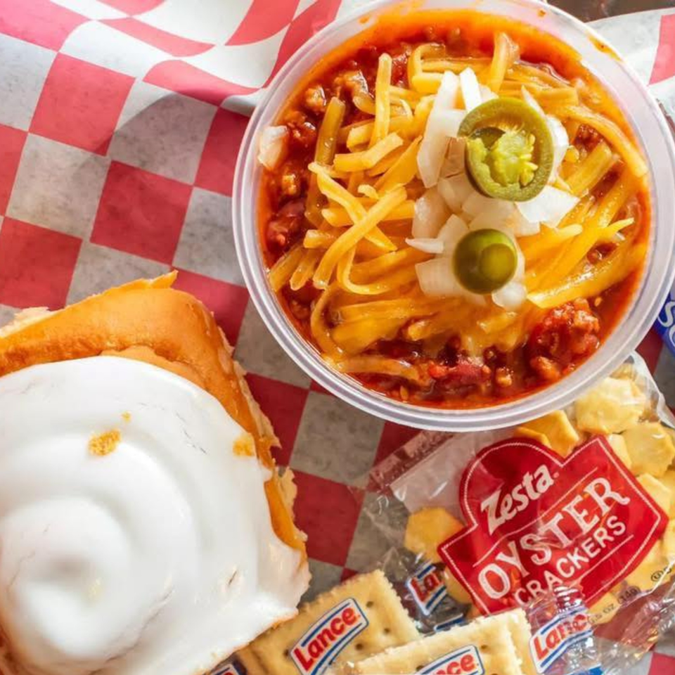A bowl of chili with cheese, onions, and jalapeños, alongside a cinnamon roll and oyster crackers.