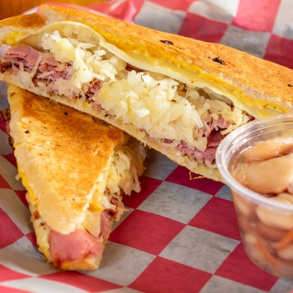 A grilled Reuben sandwich with corned beef and sauerkraut, served with a side of pickled vegetables.