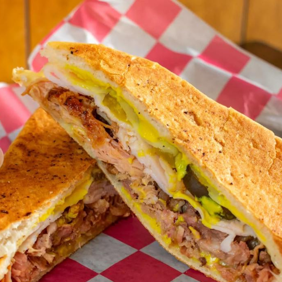 A toasted Cuban sandwich, cut in half, revealing layers of meat, cheese, mustard, and pickles.