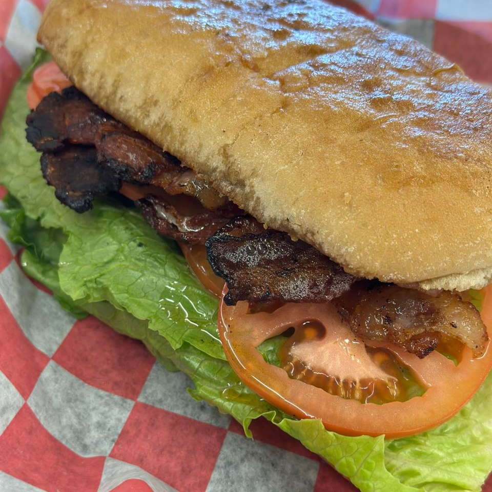 A Little Russia Chili Parlor sandwich with bacon, lettuce, and tomato on a red and white checkered paper.