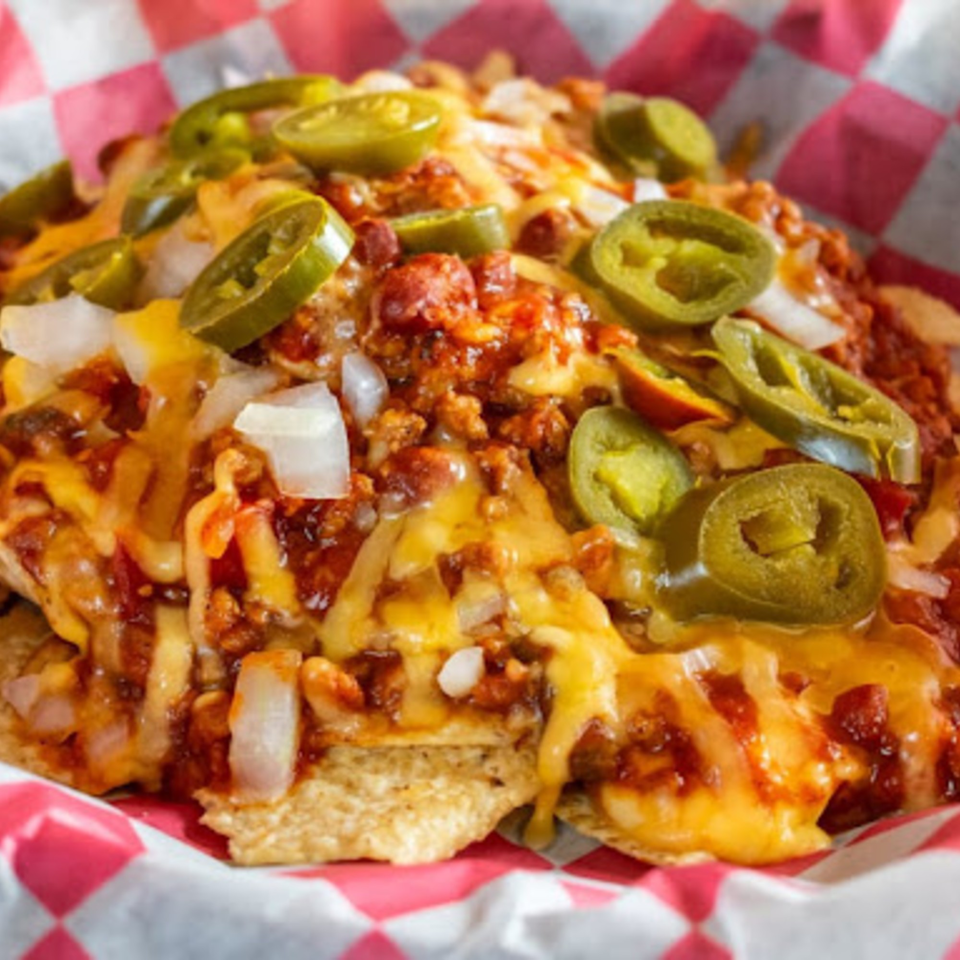Chili cheese nachos with jalapeños and diced onions in a red and white checkered basket.